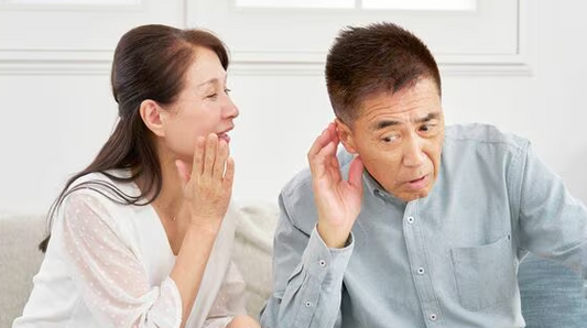 話しかける女性と聞こえにくそうに耳に手を当てる男性