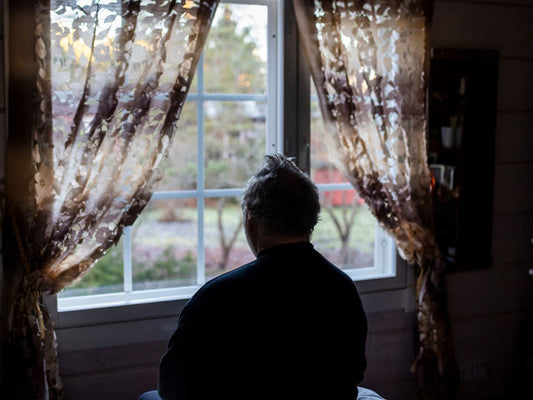 暗い部屋から外を見つめる年配の男性Milamai/Getty Images